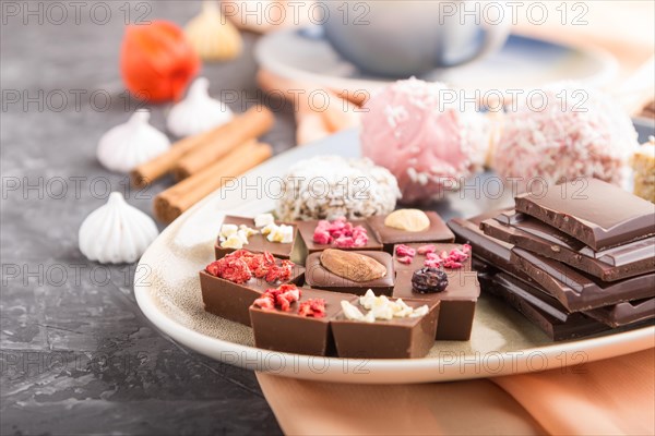 A pieces of homemade chocolate with coconut candies and a cup of coffee on a black concrete background and orange textile. side view, close up, selective focus