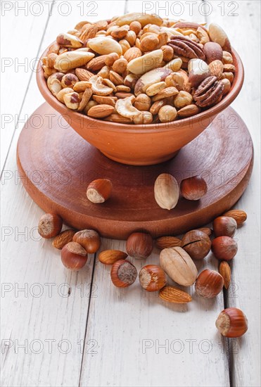 Mixed different kinds of nuts in ceramic bowl on white wooden background. hazelnut, brazil nut, almond, pumpkin seeds, cashew. close up