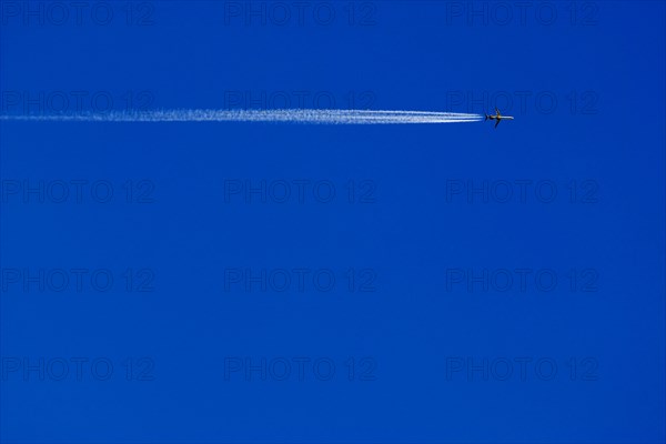 A passenger plane with vapour trail high in the blue sky