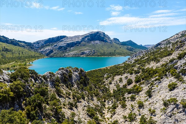 A picturesque lake surrounded by rocky mountains and green vegetation under a bright blue sky, Majorca