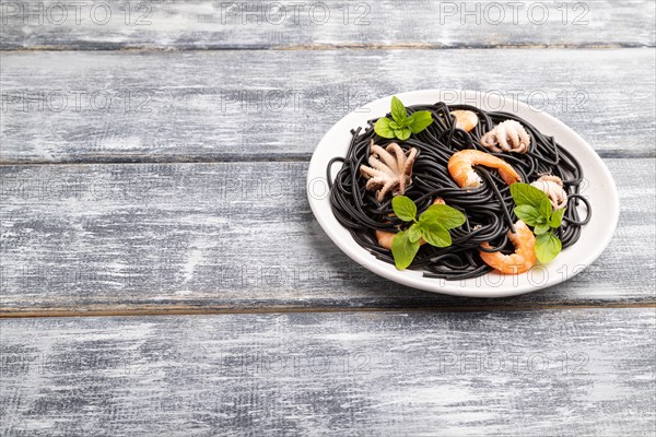 Black cuttlefish ink pasta with shrimps or prawns and small octopuses on gray wooden background. Side view, copy space