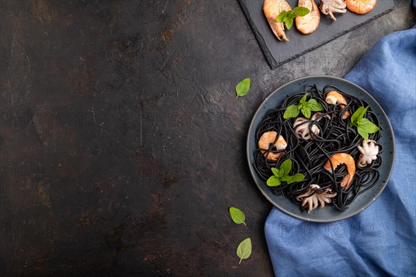 Black cuttlefish ink pasta with shrimps or prawns and small octopuses on black concrete background and blue textile. Top view, flat lay, copy space