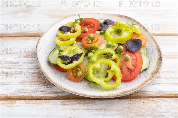 Vegetarian salad from green pea, tomatoes, pepper and basil on white wooden background. Side view, close up