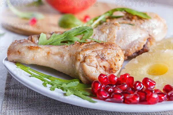 Fried chicken legs with rucola, pineapple and pomegranate seeds on white wooden background, copy space, close up
