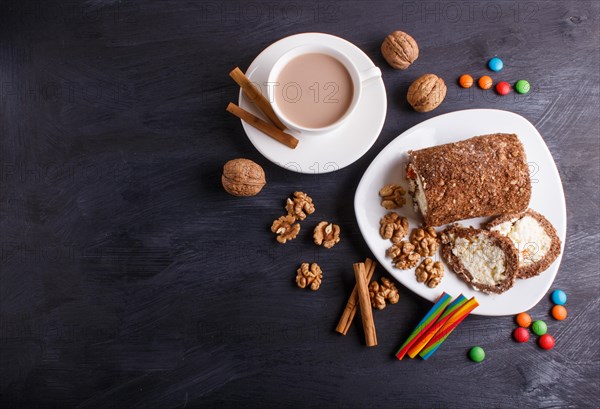 Roll cake with curd and walnuts isolated on black wooden background. top view, copy space