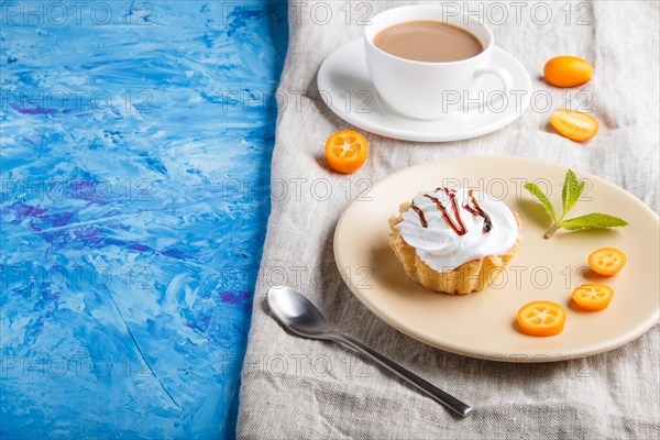 Cake with whipped egg cream on a light brown plate with kumquat slices and mint leaves on a blue concrete background with linen napkin. copy space, side view