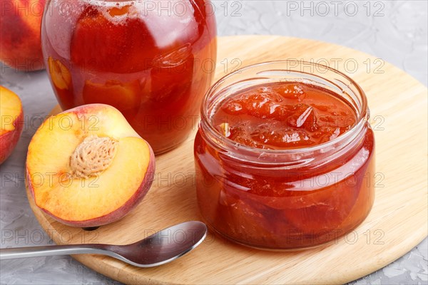 Peach jam in a glass jar with fresh fruits on gray concrete background. side view, close up