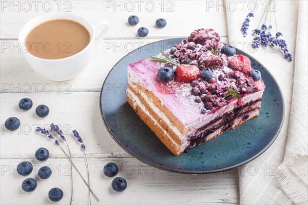 Berry cake with milk cream and blueberry jam on blue ceramic plate with cup of coffee and fresh blueberries on a white wooden background. side view, close up