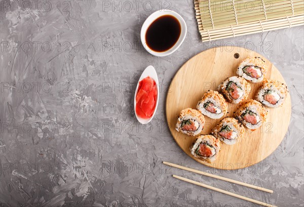 Japanese maki sushi rolls with salmon, sesame, chopsticks, soy sauce and marinated ginger on wooden board on a gray concrete background. Top view, copy space