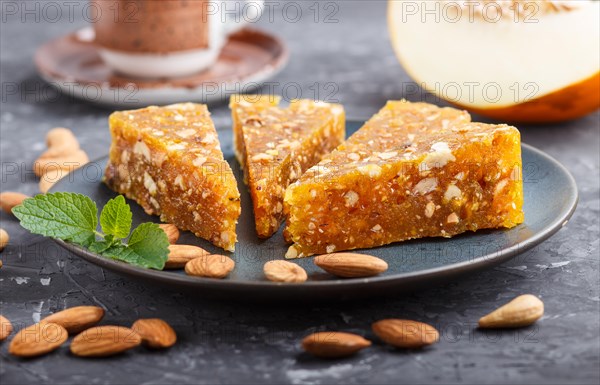 Traditional turkish candy cezerye made from caramelised melon, roasted walnuts, hazelnuts, cashew, pistachios in blue ceramic plate and a cup of coffee on a black concrete background. side view, close up, selective focus