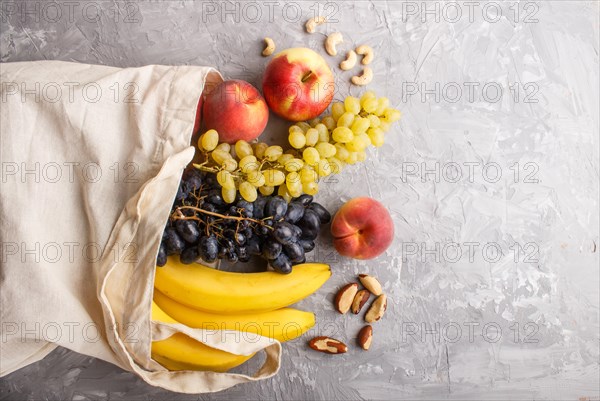 Fruits in reusable cotton textile white bag. Zero waste shopping, storage and recycling concept, eco friendly lifestyle. Top view, flat lay, copy space. Peach, apple, banana, grape