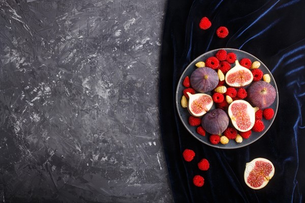 Fresh figs, strawberries and raspberries on blue ceramic plate on black concrete background and blue velvet textile. top view, flat lay, copy space