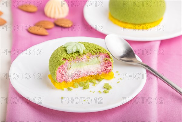 Green mousse cake with pistachio and strawberry cream on a white wooden background and pink textile. side view, close up, selective focus