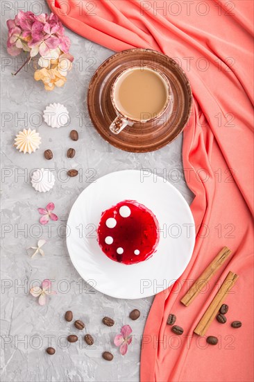 Red cake with souffle cream with cup of coffee on a gray concrete background and red textile. top view, flat lay, close up