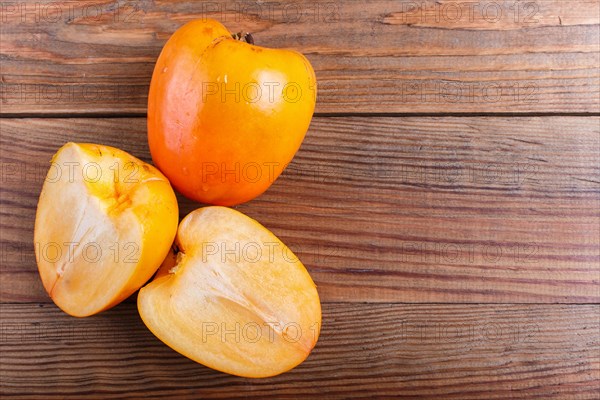 Ripe orange persimmon on brown wooden background, with copy space, top view