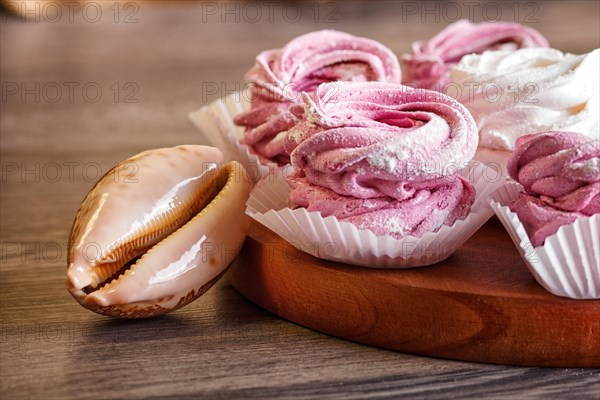 Pink and white homemade marshmallows (zephyr) on a round wooden board with seashells on a gray wooden background