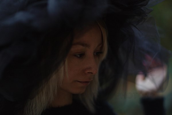 Profile view of a contemplative woman wearing a moody tulle hat in dim lighting