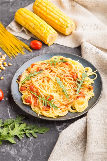 Corn noodles with tomato sauce and arugula on a black concrete background and linen textile. Side view, close up, selective focus