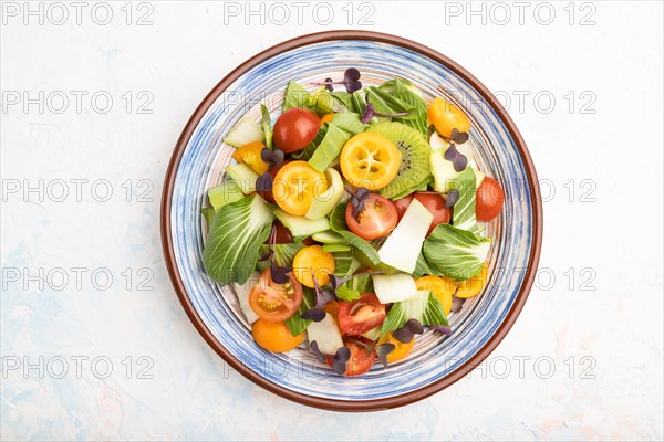 Vegetarian salad of pac choi cabbage, kiwi, tomatoes, kumquat, microgreen sprouts on a white concrete background. Top view, flat lay, close up