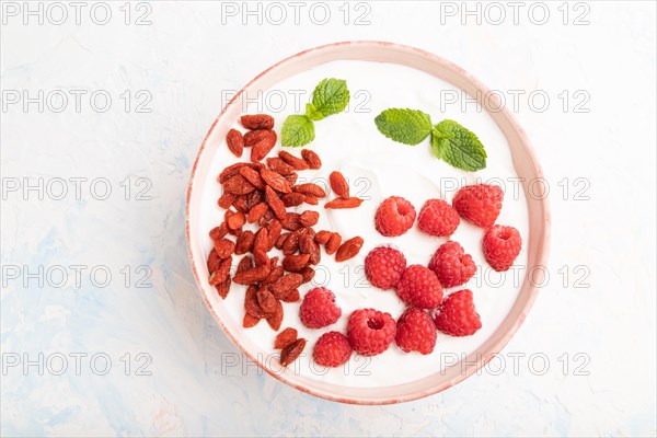 Yogurt with raspberry and goji berries in ceramic bowl on white concrete background. top view, flat lay, close up