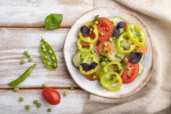 Vegetarian salad from green pea, tomatoes, pepper and basil on white wooden background and linen textile. top view, close up, flat lay
