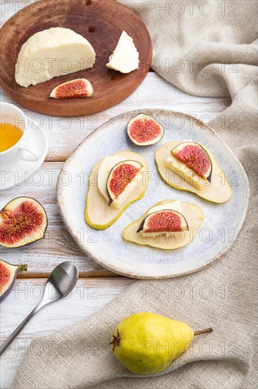 Summer appetizer with pear, cottage cheese, figs and honey on a white wooden background and linen textile. Side view, close up