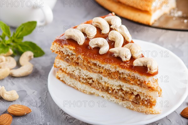 Piece of homemade cake with caramel cream and nuts with cup of coffee on a gray concrete background. side view, close up, selective focus