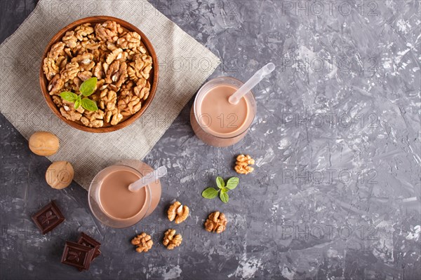 Organic non dairy walnut chocolate milk in glass and wooden plate with walnuts on a black concrete background. Vegan healthy food concept, flat lay, top view, copy space