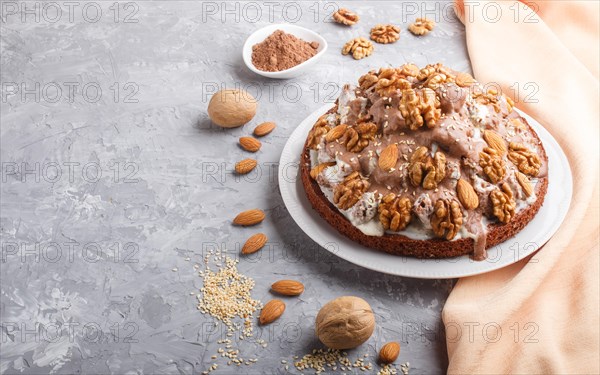 Homemade cake with milk cream, cocoa, almond, hazelnut on a gray concrete background with orange textile. Side view, copy space