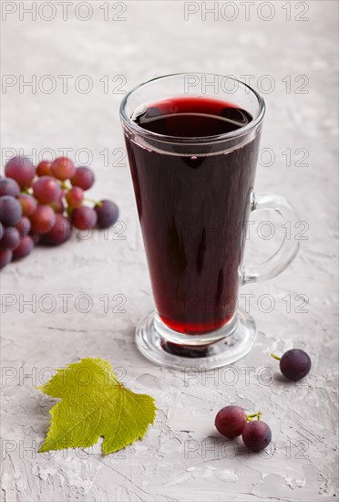 Glass of red grape juice on a gray concrete background. Morninig, spring, healthy drink concept. Side view, close up