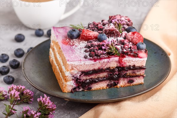 Berry cake with milk cream and blueberry jam on blue ceramic plate with cup of coffee and fresh blueberries on a gray concrete background with orange textile. side view, close up, selective focus