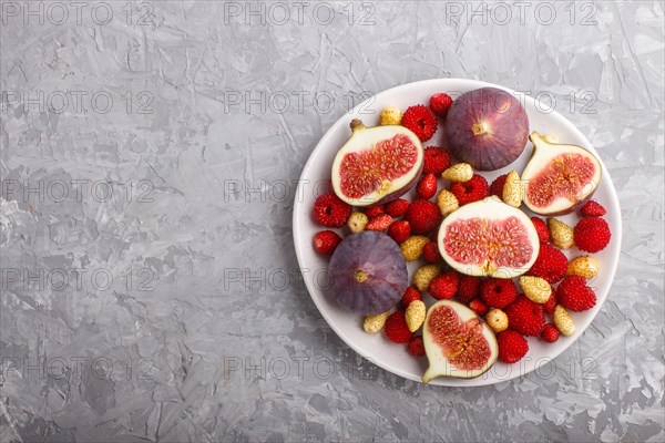 Fresh figs, strawberries and raspberries on white ceramic plate on gray concrete background. top view, flat lay, copy space