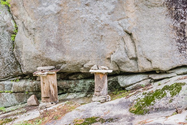 Two logs held in place with stones and carved to have one eye and mouth on rocky ledge of cliff face in countryside in South Korea