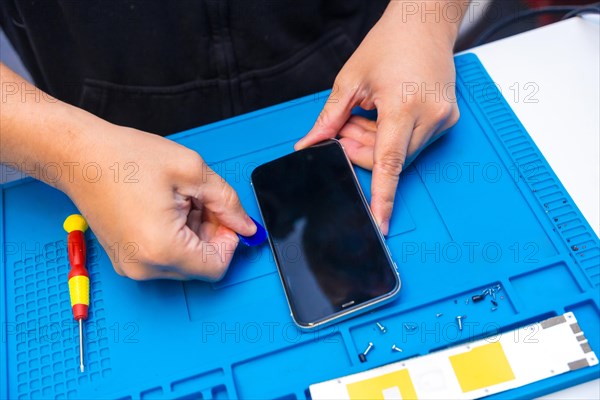 Top view close-up of the hands of a repairman opening a phone in parts using a pick in a workshop