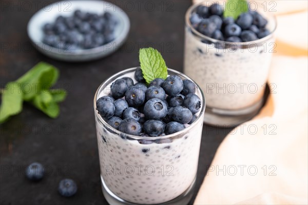 Yogurt with blueberry and chia in glass on black concrete background and orange linen textile. Side view, close up