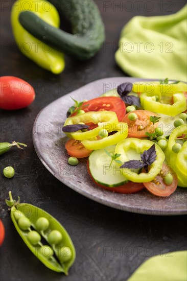 Vegetarian salad from green pea, tomatoes, pepper and basil on a black concrete background and green textile. Side view, close up, selective focus