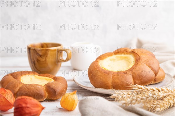 Sour cream bun with cup of coffee on a white wooden and concrete background and linen textile. Side view, close up, selective focus