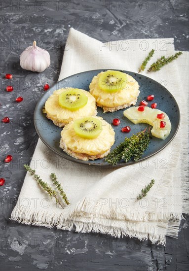 Pieces of baked pork with pineapple, cheese and kiwi on black background, side view, close up