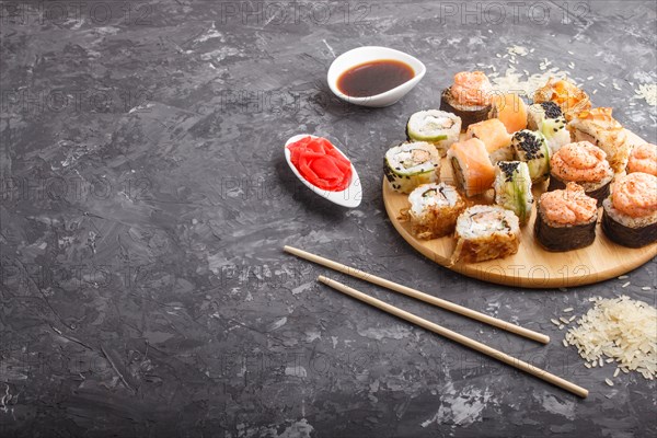 Mixed japanese maki sushi rolls set with chopsticks, ginger, soy sauce, rice on black concrete background. side view, copy space, flat lay
