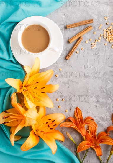 Orange day-lily and lavender flowers and a cup of coffee on a gray concrete background, with blue textile. Morninig, spring, fashion composition. Flat lay, top view, copy space