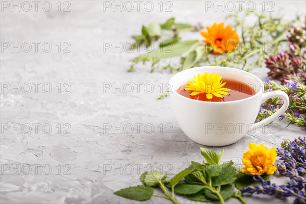 Cup of herbal tea with calendula, lavender, oregano, hyssop, mint and lemon balm on a gray concrete background. Morninig, spring, healthy drink concept. Side view, selective focus, copy space