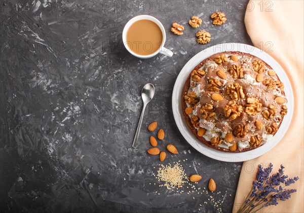 Homemade cake with milk cream, cocoa, almond, hazelnut on a black concrete background with orange textile and a cup of coffee. Top view, flat lay, copy space