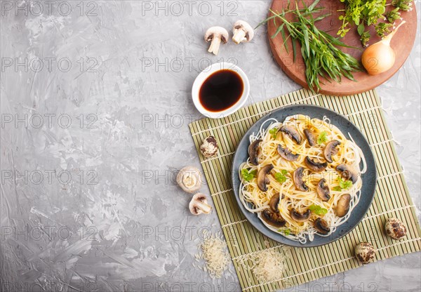 Rice noodles with champignons mushrooms, egg sauce and oregano on blue ceramic plate on a gray concrete background. Top view, flat lay, copy space