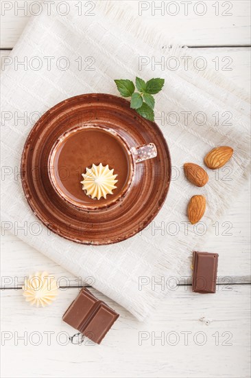 Cup of hot chocolate and pieces of milk chocolate with almonds on a white wooden background with linen napkin. top view, flat lay, close up