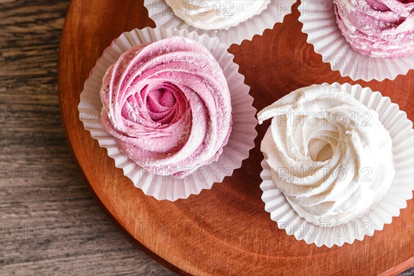 Pink and white marshmallows on a round wooden board on a gray wooden background. selective focus