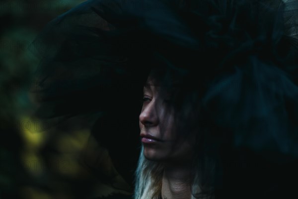 A white thin caucasian blonde woman in shadows wears a large hat, creating a moody and introspective scene