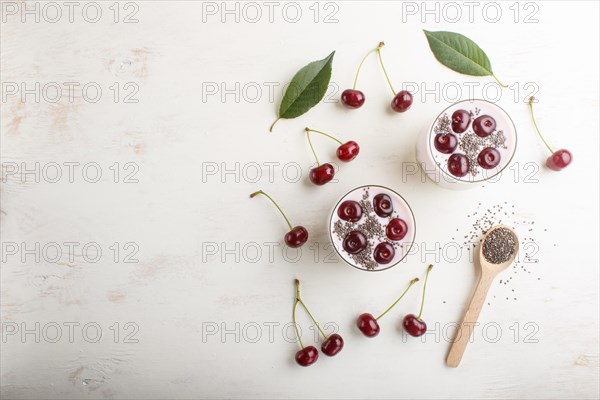 Yoghurt with cherries, chia seeds and granola in glass with wooden spoon on white wooden background. top view, copy space, flat lay