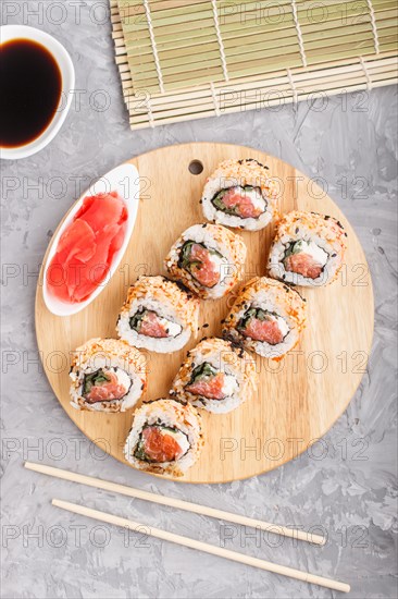 Japanese maki sushi rolls with salmon, sesame, chopsticks, soy sauce and marinated ginger on wooden board on a gray concrete background. Top view, flat lay