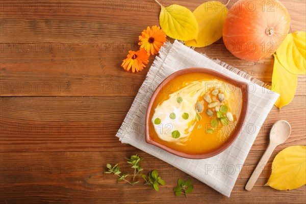 Traditional pumpkin cream soup with seeds in clay bowl on a brown wooden background with linen napkin. top view, flat lay, copy space