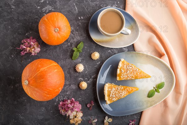 Two pieces of traditional american pumpkin pie with cup of coffee and pumpkins on a black concrete background and orange textile. top view, flat lay, contrast